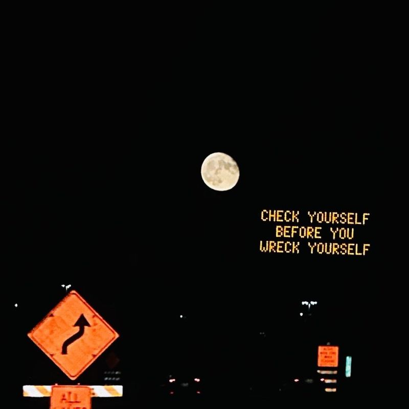 Full moon above a highway sign reading "Check yourself before you wreck yourself"